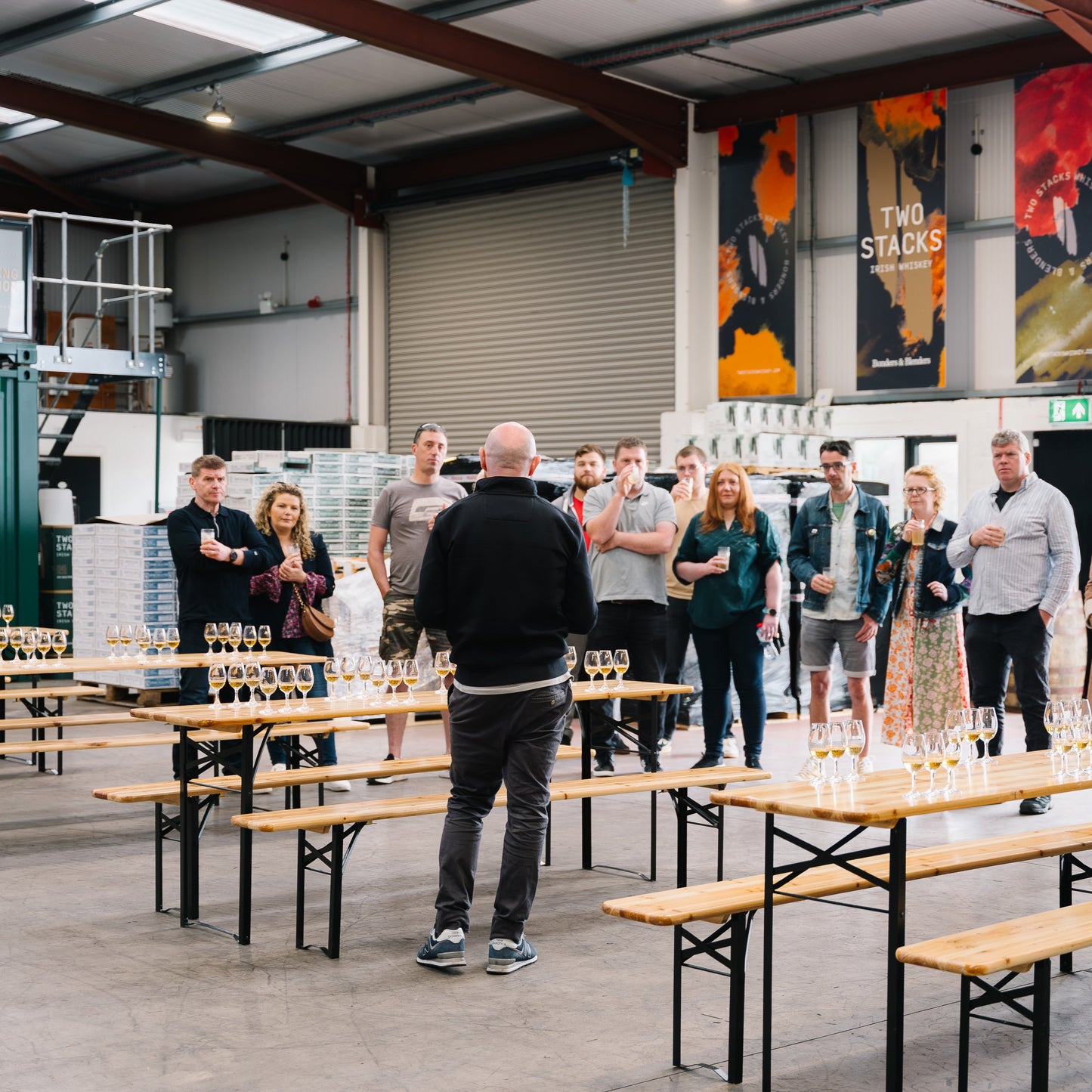 Group of people standing around tables in a warehouse setting with 'Two Stacker' branding.