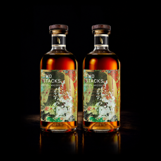 Two bottles of Two Stacks Whiskey with colorful illustrated labels, set against a solid black background with a reflective surface below.
