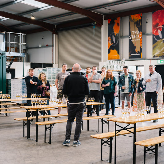 Group of people standing around tables in a warehouse setting with 'Two Stacker' branding.